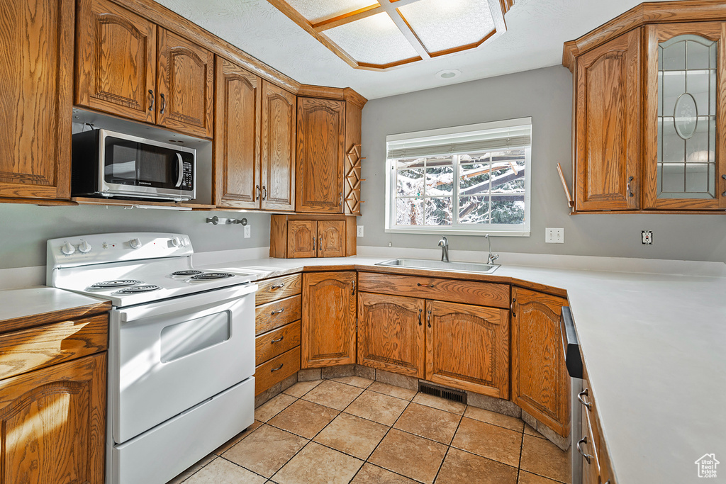 Kitchen with stainless steel microwave, light countertops, brown cabinetry, white electric range, and a sink