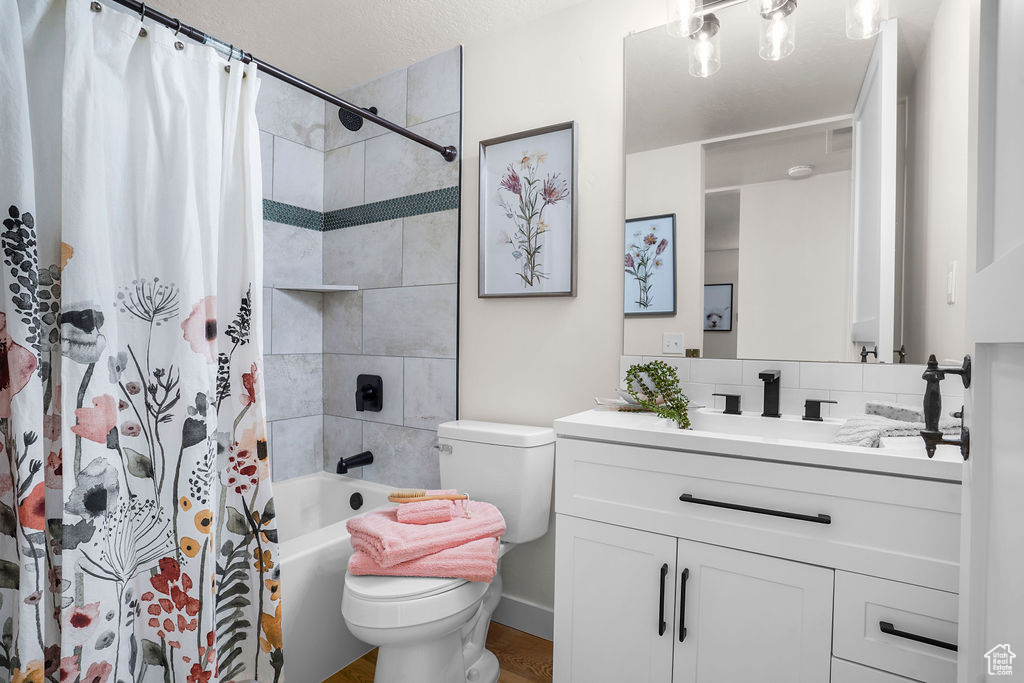 Bathroom with tasteful backsplash, vanity, toilet, and shower / bath combo with shower curtain