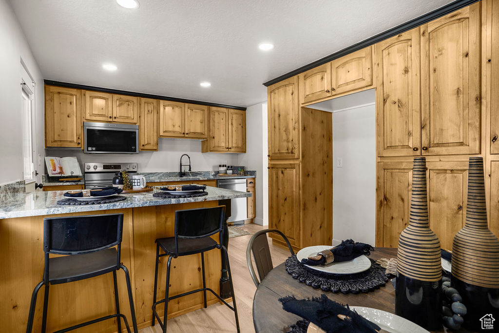 Kitchen with stone counters, a breakfast bar, light wood-style flooring, a sink, and appliances with stainless steel finishes