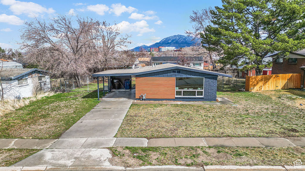 View of front of house with an attached carport, a front lawn, fence, concrete driveway, and a mountain view