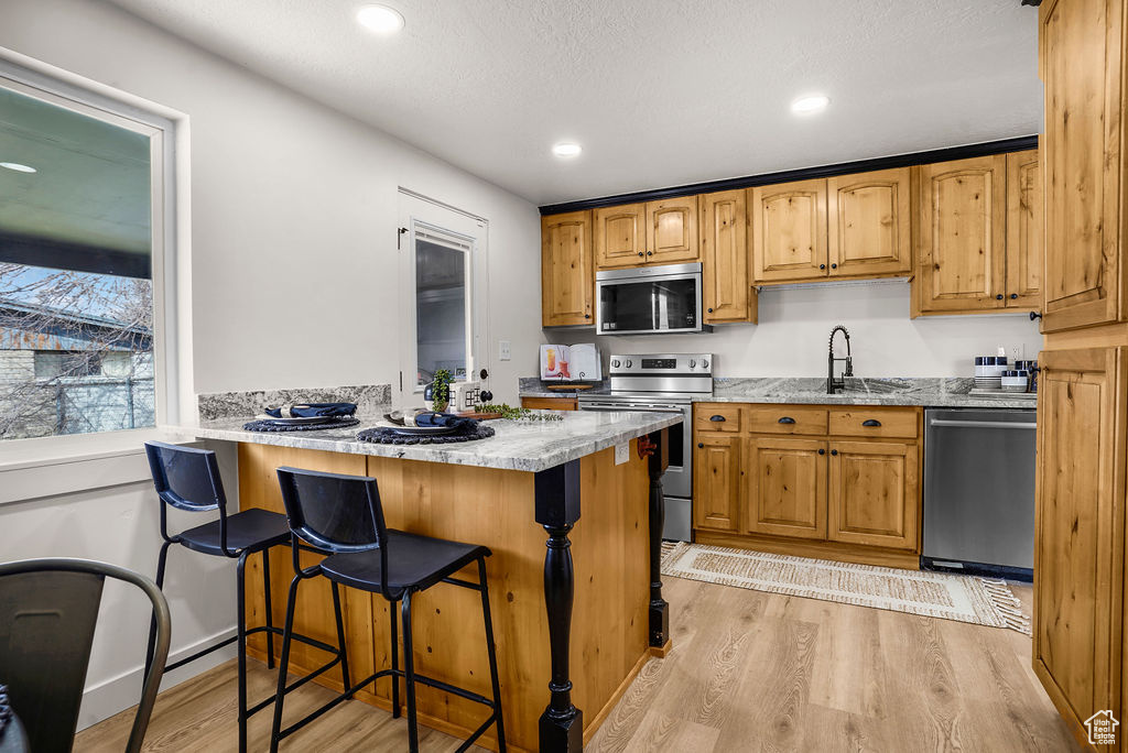 Kitchen featuring light stone counters, a sink, light wood-style floors, appliances with stainless steel finishes, and a kitchen bar