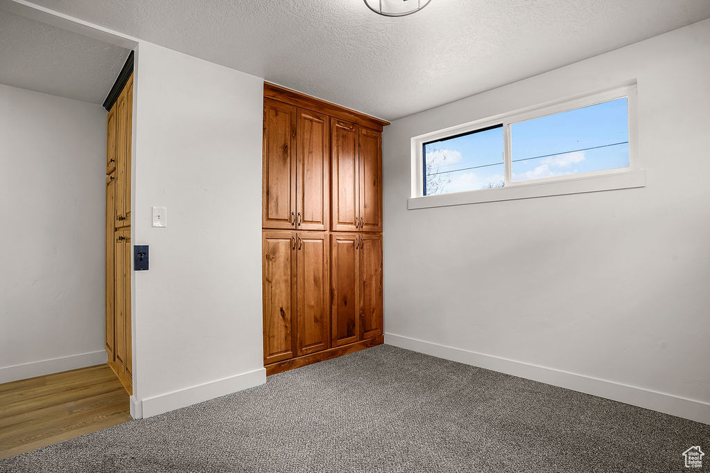 Unfurnished bedroom featuring light colored carpet, baseboards, and a textured ceiling