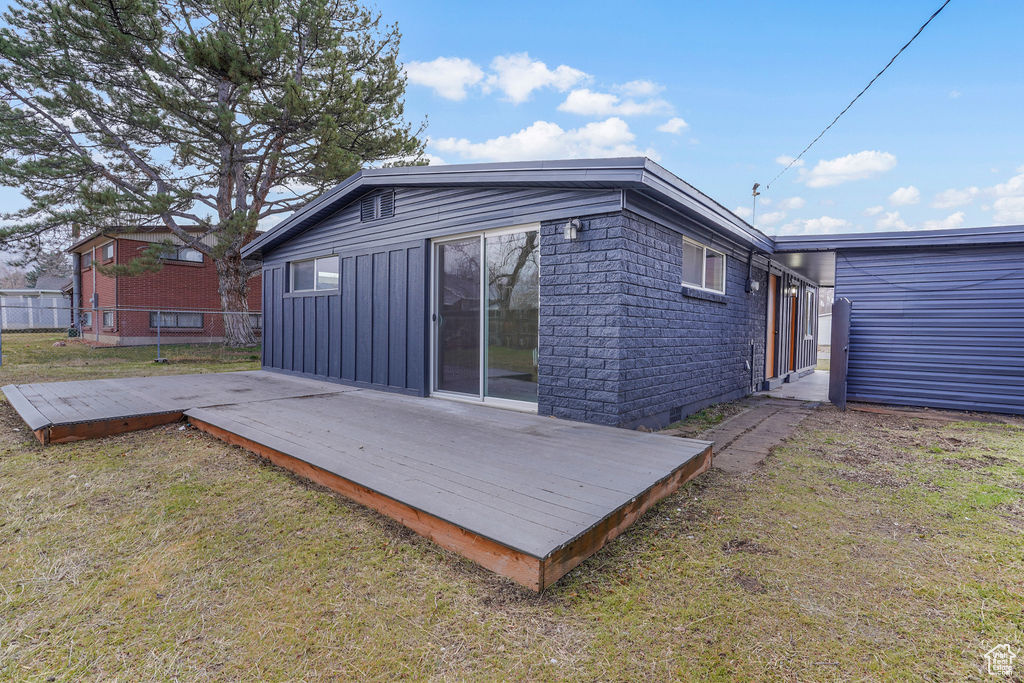 Back of property with a lawn, board and batten siding, a deck, and fence