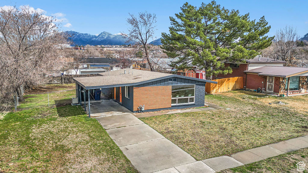 Mid-century inspired home with a carport, concrete driveway, fence, and a front yard