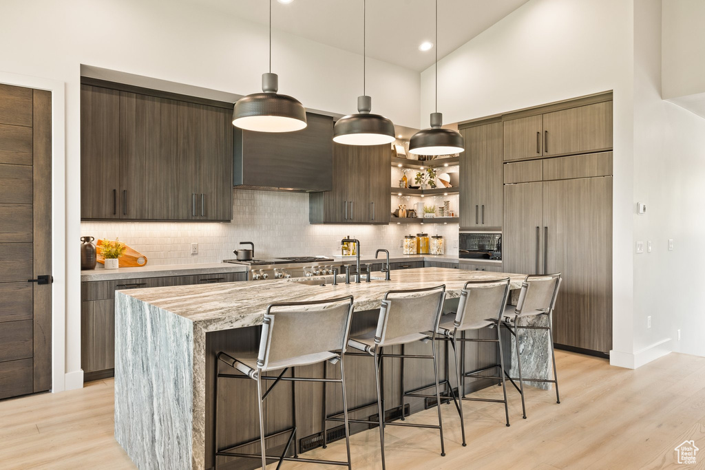 Kitchen with wall chimney exhaust hood, modern cabinets, paneled fridge, a breakfast bar, and decorative backsplash