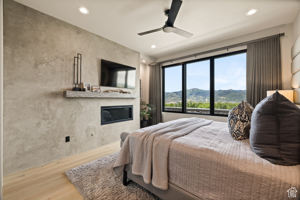Bedroom with wood finished floors, a glass covered fireplace, recessed lighting, and a ceiling fan