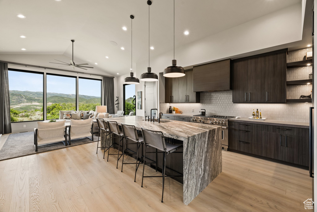 Kitchen featuring high end stainless steel range oven, open shelves, wall chimney exhaust hood, a ceiling fan, and a kitchen breakfast bar