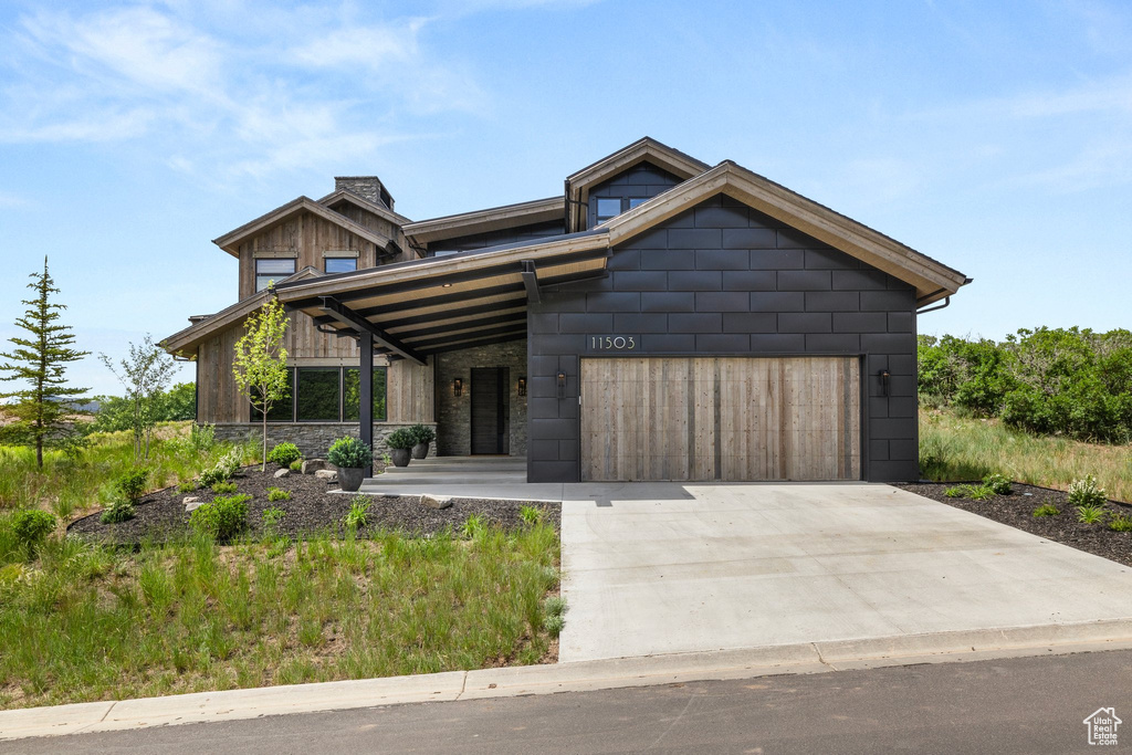 View of front facade with an attached garage, a chimney, driveway, and stone siding