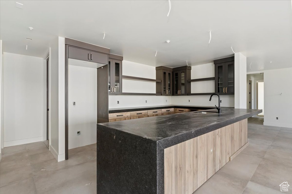 Kitchen with a sink, open shelves, concrete flooring, glass insert cabinets, and a spacious island