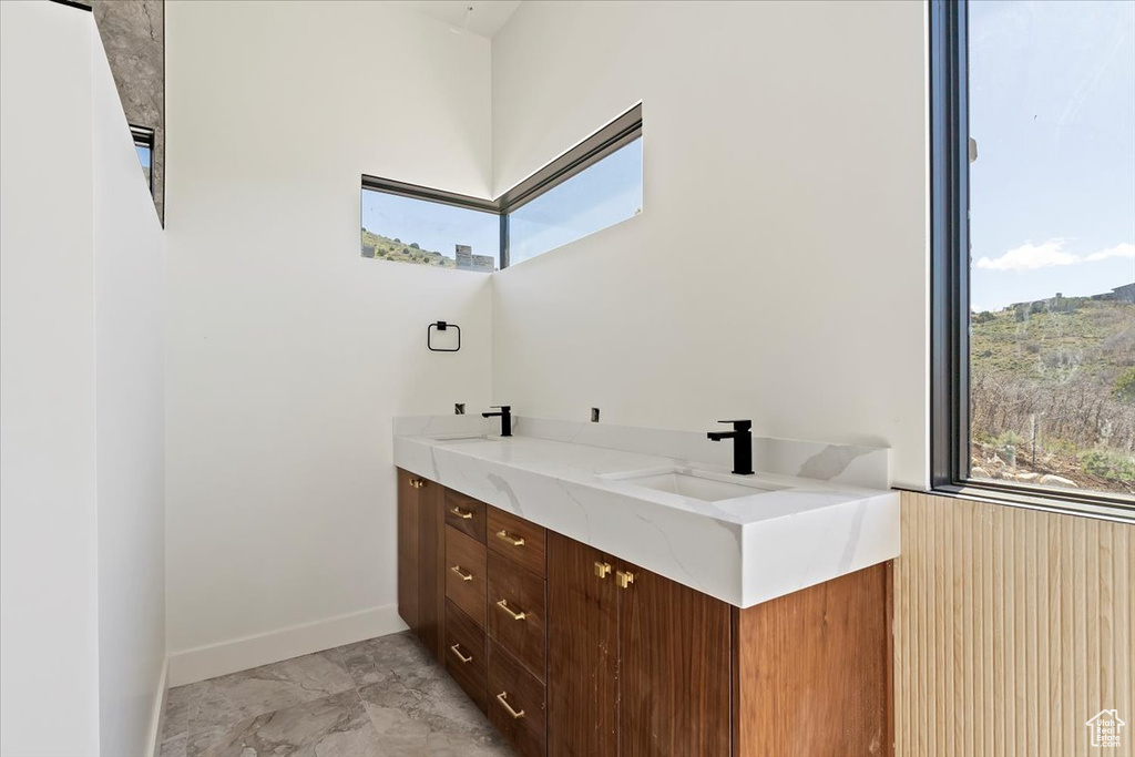Bathroom featuring plenty of natural light, marble finish flooring, baseboards, and double vanity