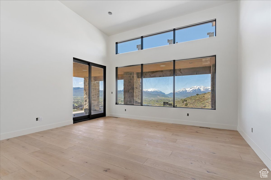 Unfurnished room with a towering ceiling, light wood-style flooring, and baseboards