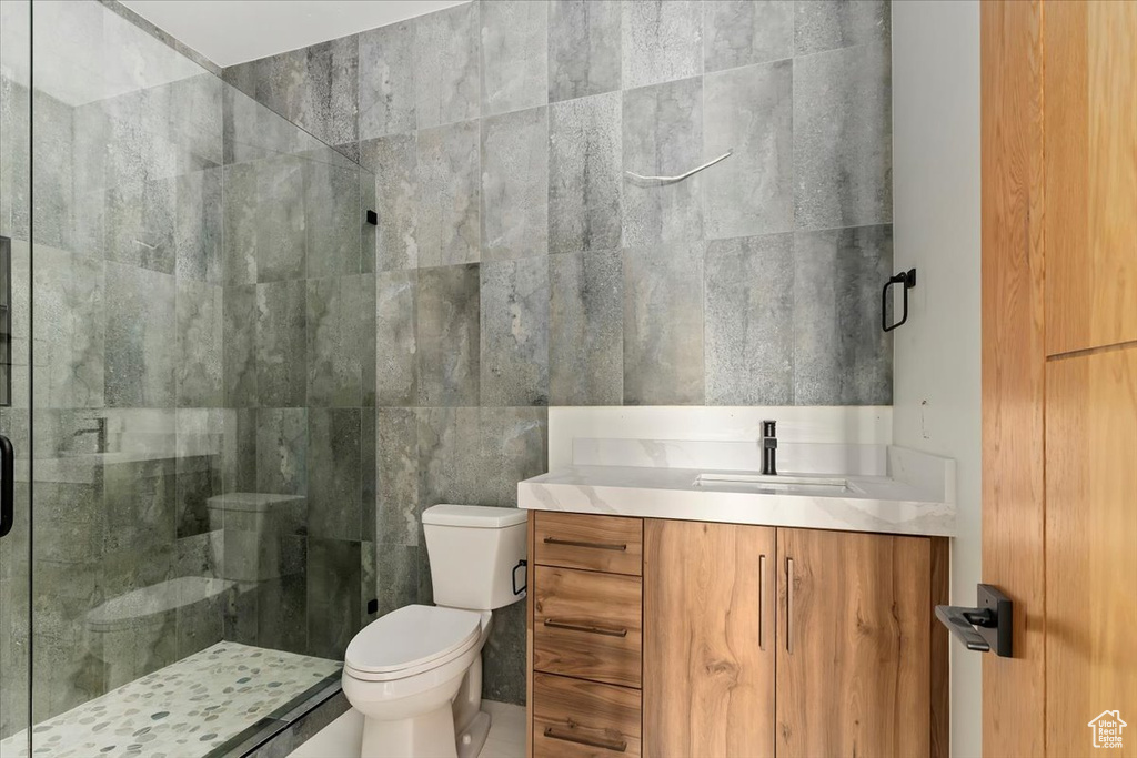 Bathroom featuring toilet, a shower stall, vanity, and tile walls