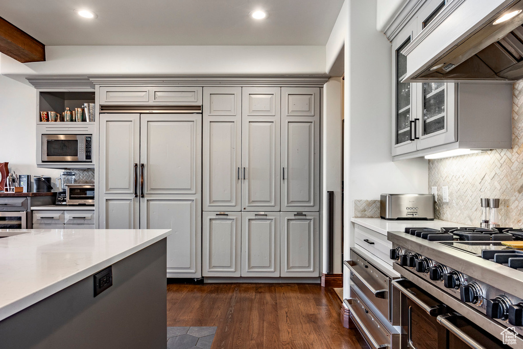 Kitchen featuring light countertops, built in appliances, backsplash, and under cabinet range hood