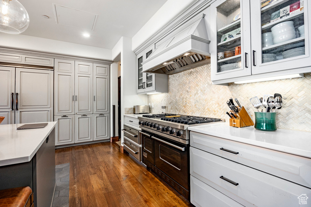 Kitchen featuring light countertops, premium range hood, high end appliances, backsplash, and glass insert cabinets