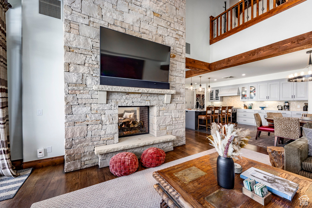 Living area with a towering ceiling, a stone fireplace, baseboards, dark wood-style floors, and a chandelier