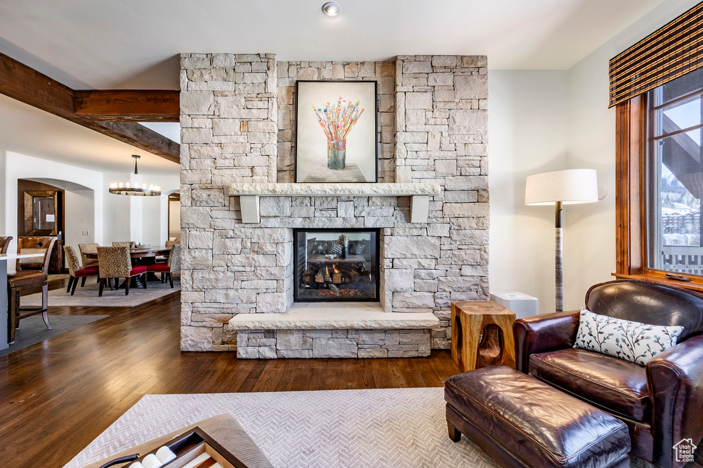 Living room featuring arched walkways, a notable chandelier, a stone fireplace, and wood finished floors