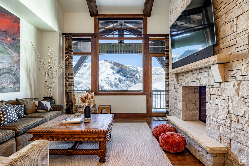 Living area featuring baseboards, beam ceiling, a stone fireplace, and wood finished floors