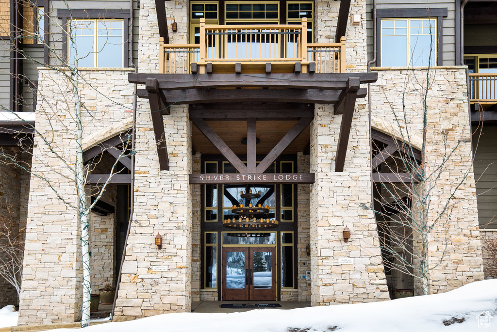 Snow covered property entrance featuring french doors, a balcony, and stone siding