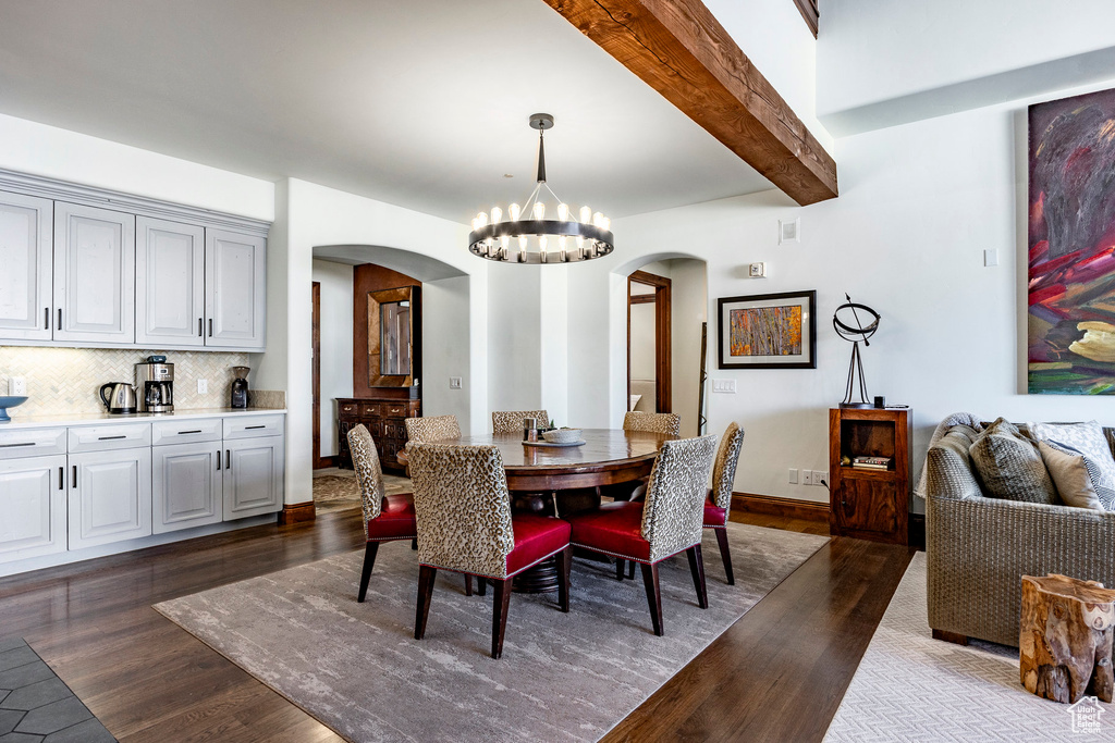 Dining area with arched walkways, a chandelier, dark wood-style floors, and beamed ceiling