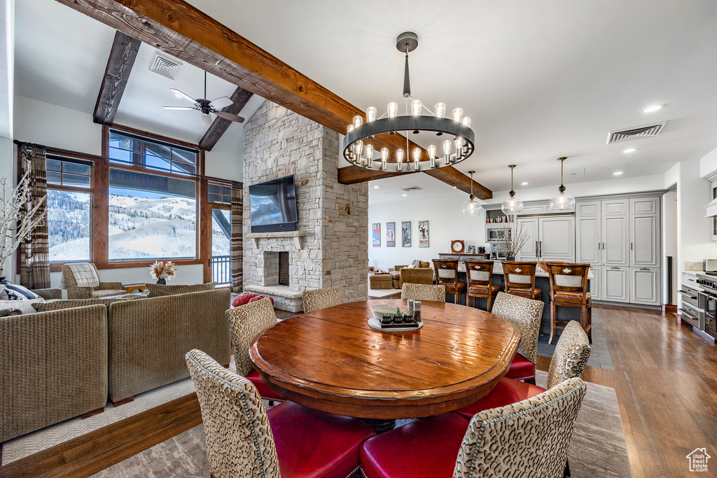 Dining area featuring visible vents, dark wood-type flooring, ceiling fan with notable chandelier, and a fireplace