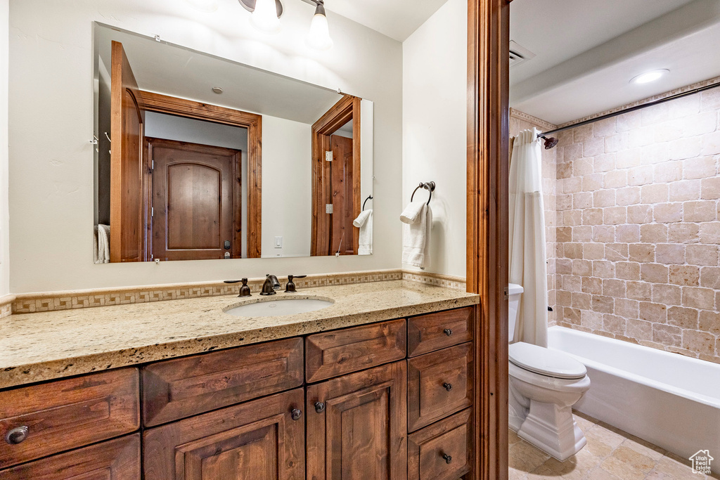 Bathroom featuring vanity, shower / bath combination with curtain, and toilet