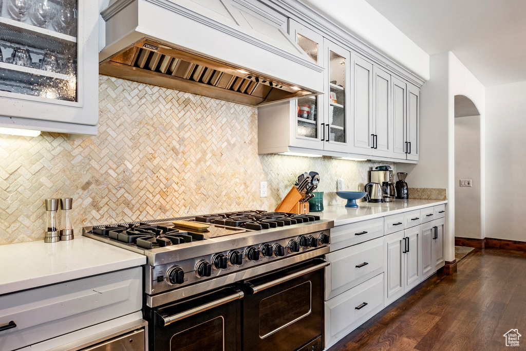 Kitchen with arched walkways, decorative backsplash, double oven range, custom range hood, and dark wood-style floors