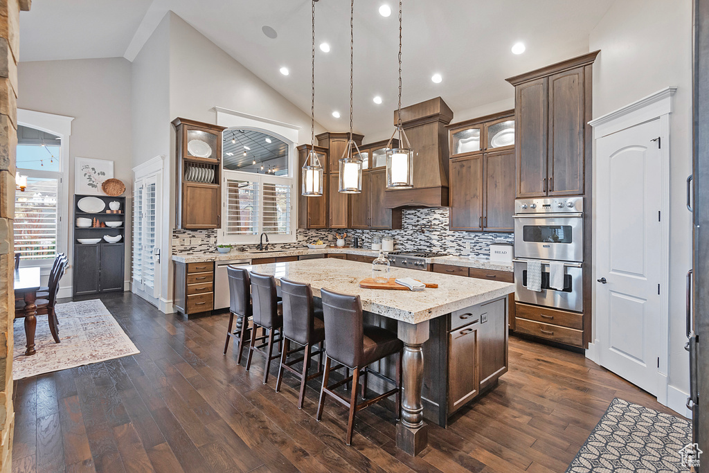 Kitchen featuring appliances with stainless steel finishes, a kitchen island, tasteful backsplash, a kitchen bar, and dark wood finished floors