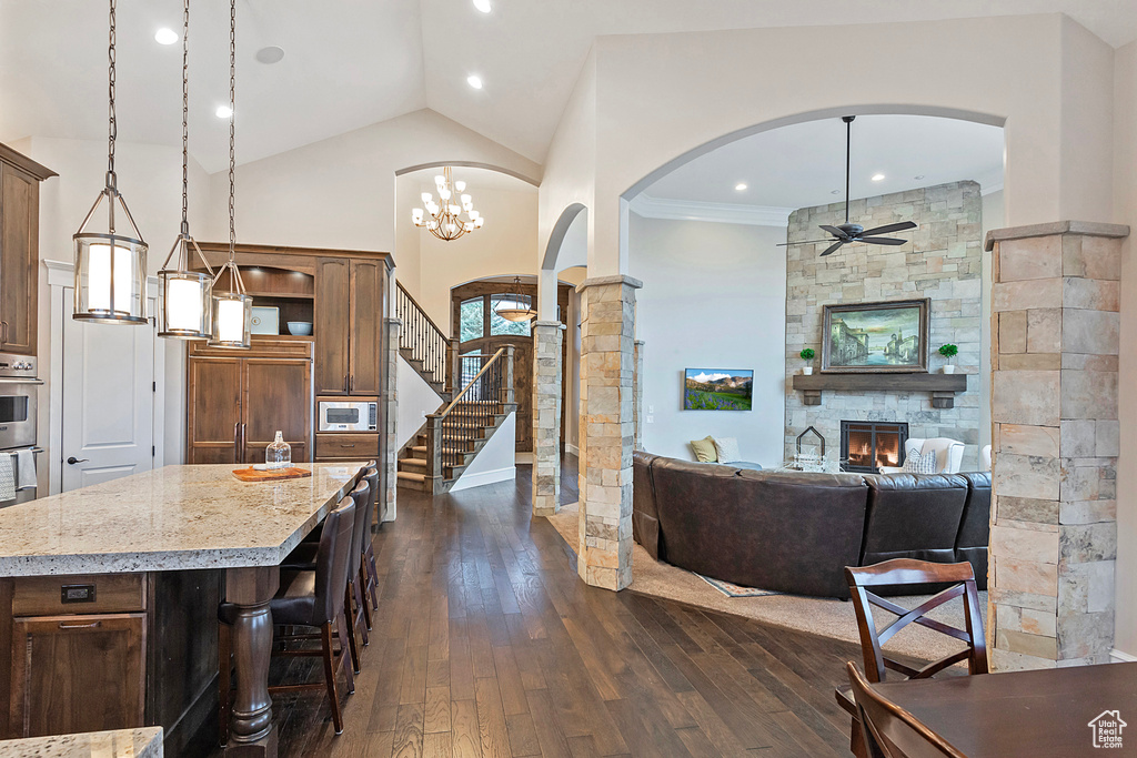 Living room featuring a ceiling fan, arched walkways, dark wood-style flooring, a fireplace, and decorative columns