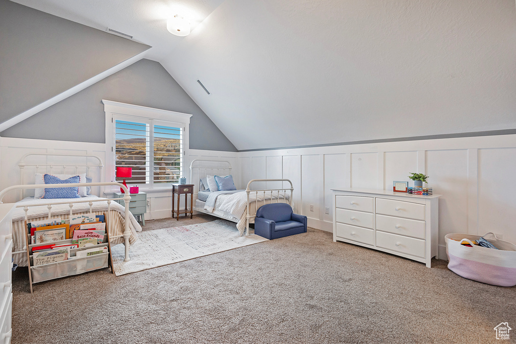 Bedroom with a decorative wall, carpet, vaulted ceiling, and a wainscoted wall