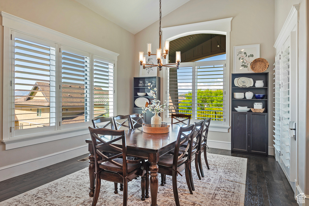 Dining area featuring a chandelier, lofted ceiling, dark wood-style flooring, and baseboards