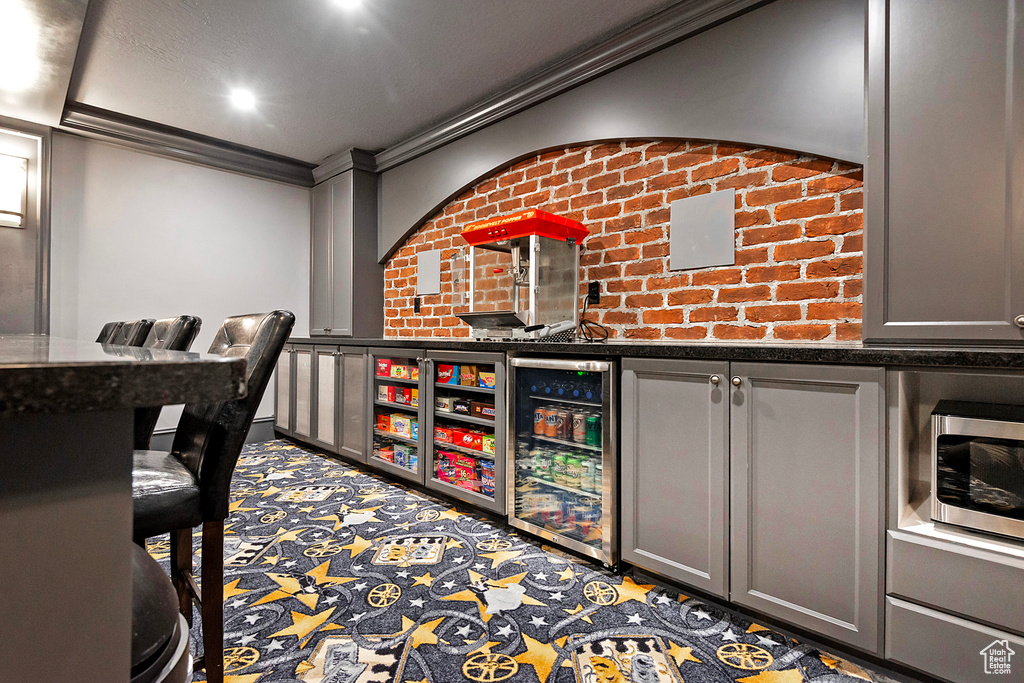 Wine cellar with wine cooler, crown molding, and a community bar
