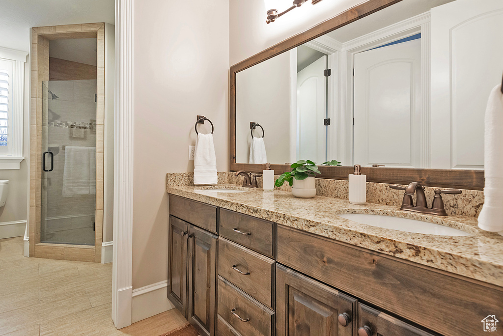 Bathroom featuring a stall shower, double vanity, and baseboards
