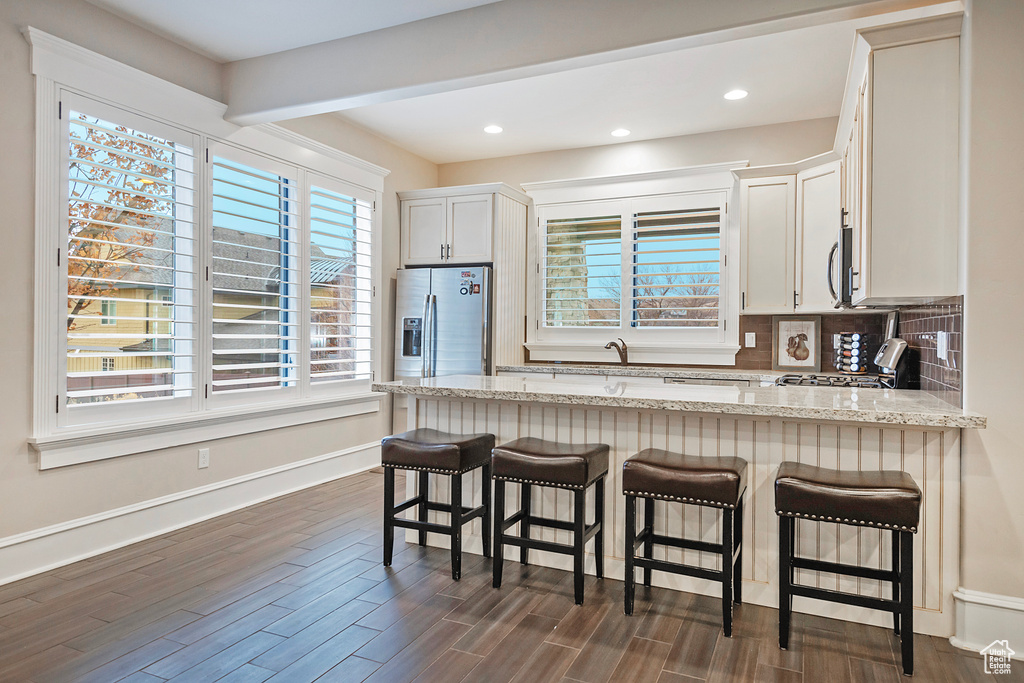 Kitchen featuring appliances with stainless steel finishes, light stone countertops, a peninsula, dark wood-style floors, and tasteful backsplash