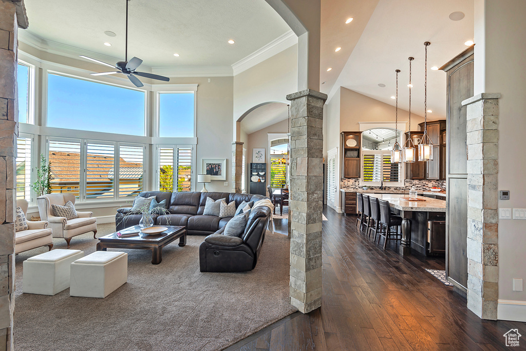 Living room with ornate columns, a ceiling fan, arched walkways, dark wood-style flooring, and ornamental molding