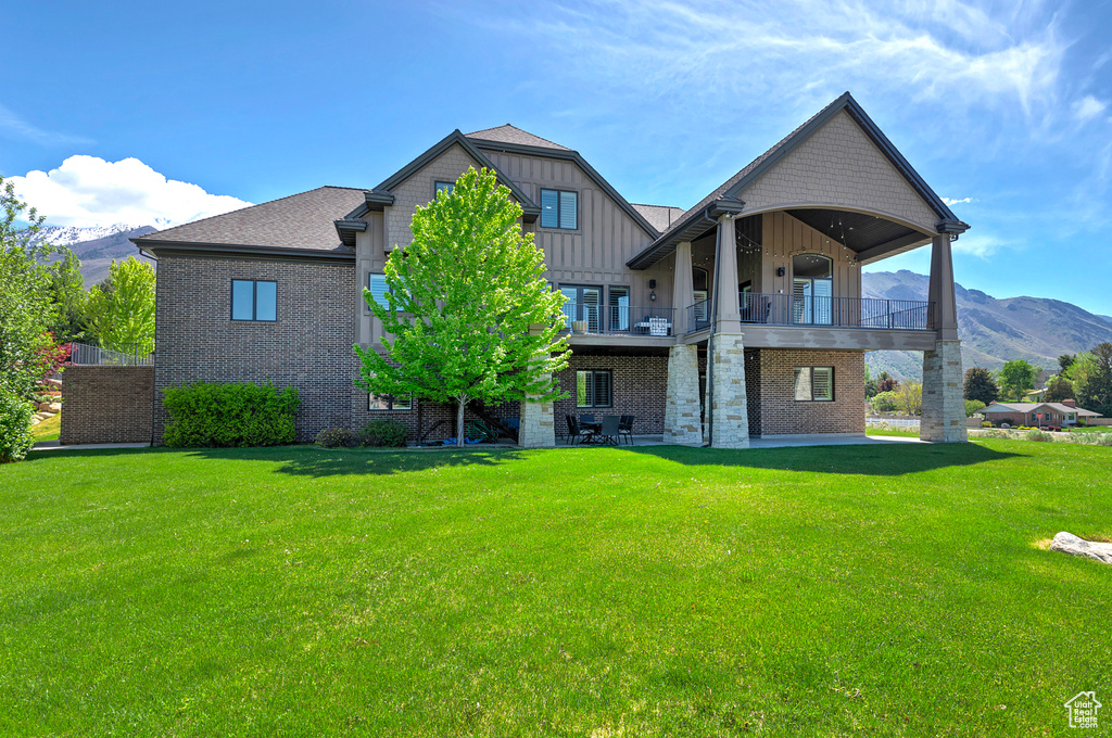 Back of house featuring a mountain view, a balcony, and a yard
