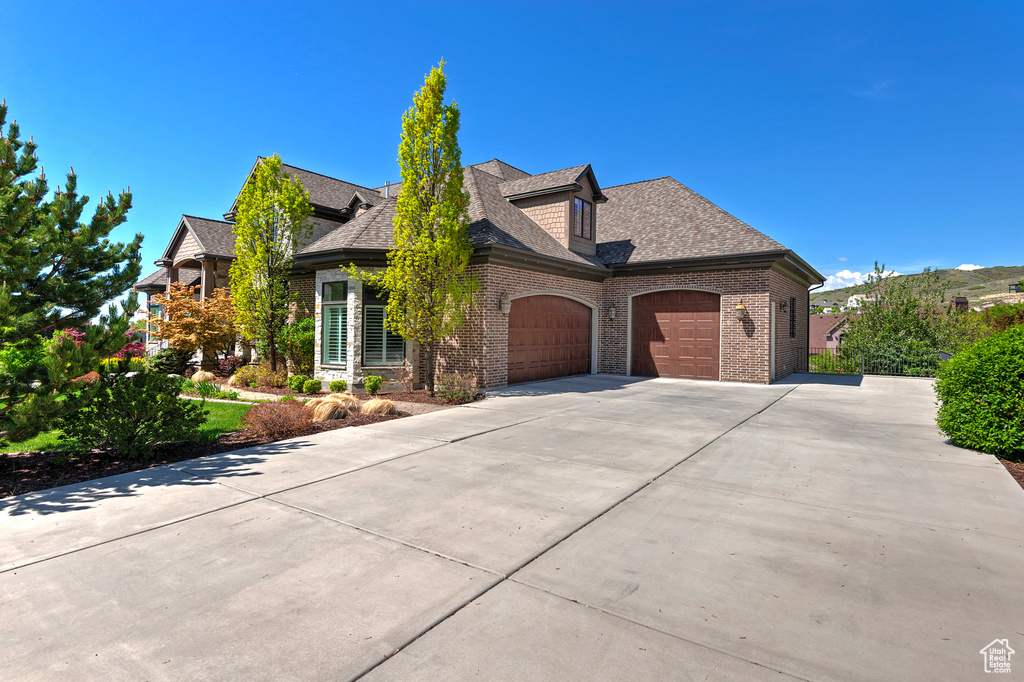 View of front of home featuring a garage, brick siding, driveway, and a shingled roof