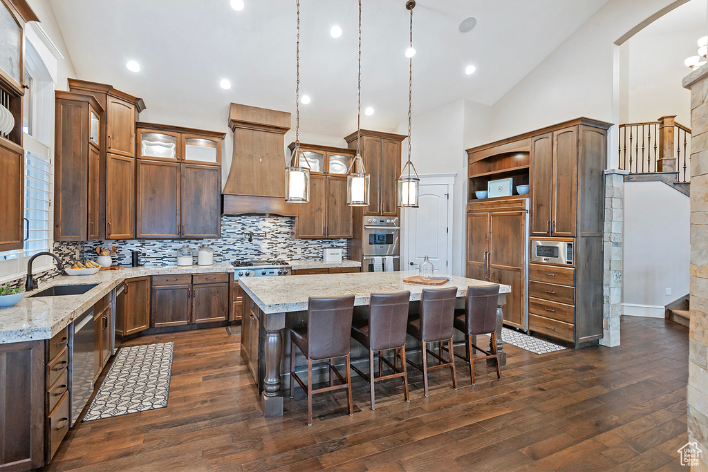 Kitchen featuring built in appliances, open shelves, a center island, a sink, and dark wood finished floors