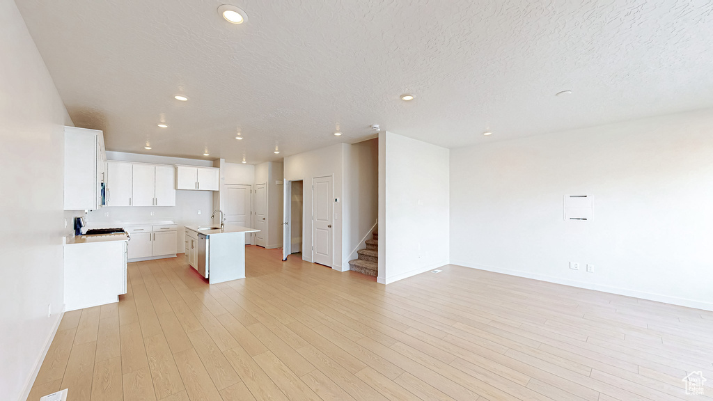 Kitchen with light wood finished floors, a kitchen island with sink, a sink, light countertops, and open floor plan