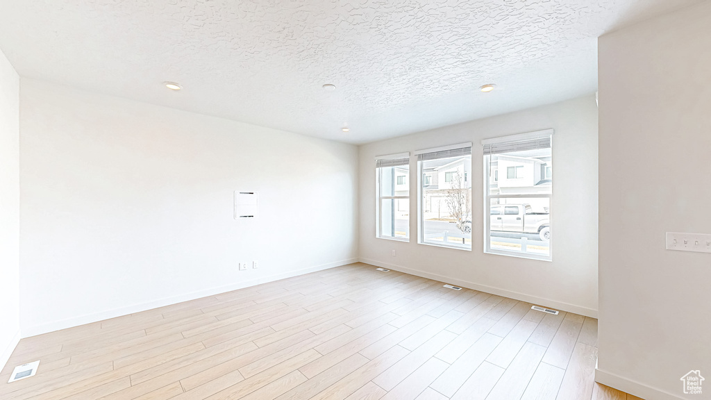 Spare room with light wood-style flooring, a textured ceiling, and baseboards