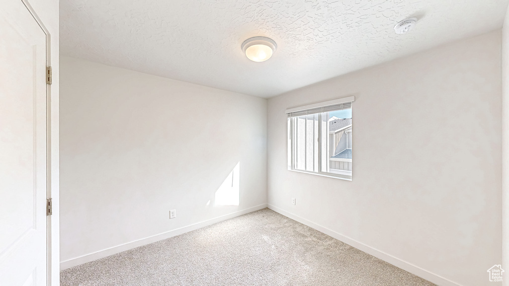 Spare room featuring light carpet, a textured ceiling, and baseboards