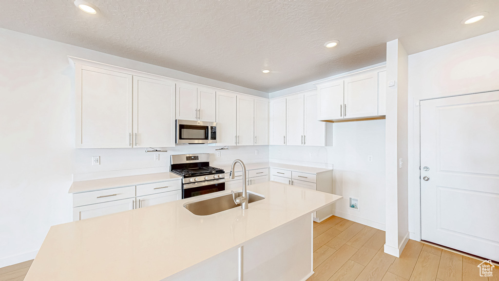 Kitchen featuring light wood finished floors, white cabinets, stainless steel appliances, and a sink