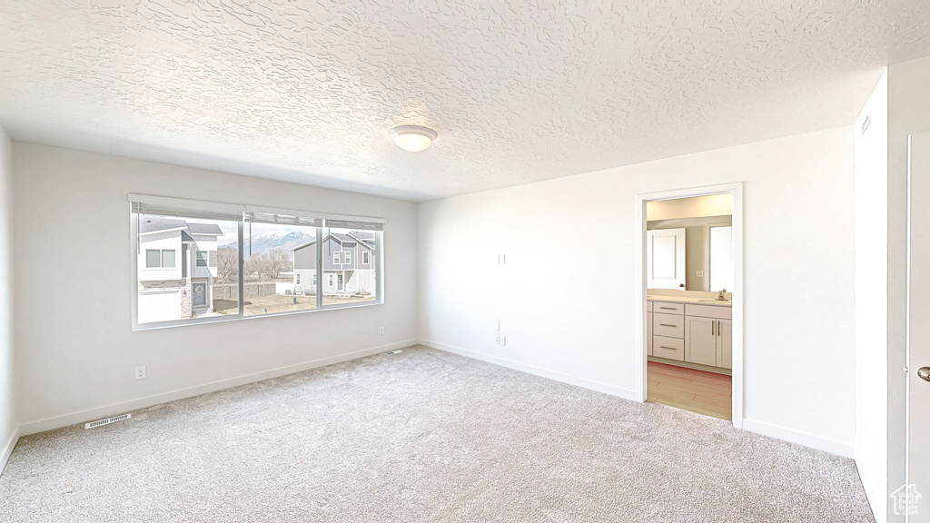 Unfurnished bedroom featuring visible vents, light carpet, ensuite bathroom, a textured ceiling, and baseboards