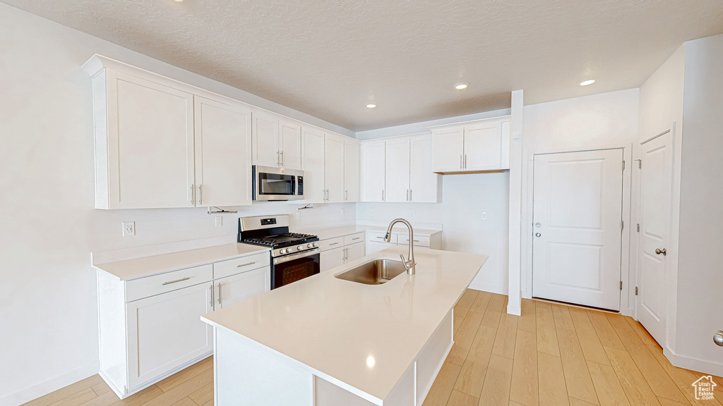 Kitchen featuring white cabinets, stainless steel appliances, light wood-type flooring, and a sink