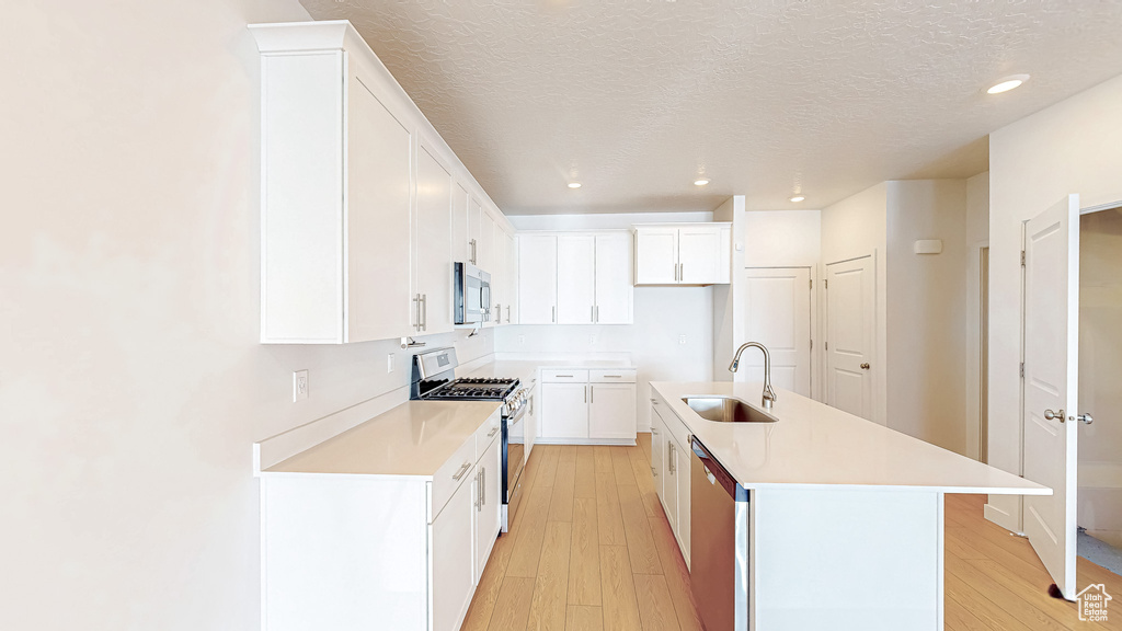 Kitchen featuring light countertops, light wood-style flooring, appliances with stainless steel finishes, white cabinetry, and a sink