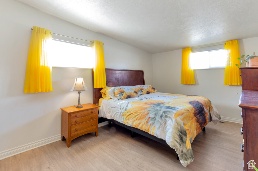Bedroom featuring baseboards, light wood-style floors, and vaulted ceiling