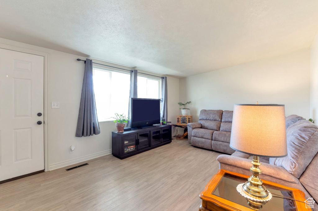 Living area with visible vents, a textured ceiling, baseboards, and wood finished floors