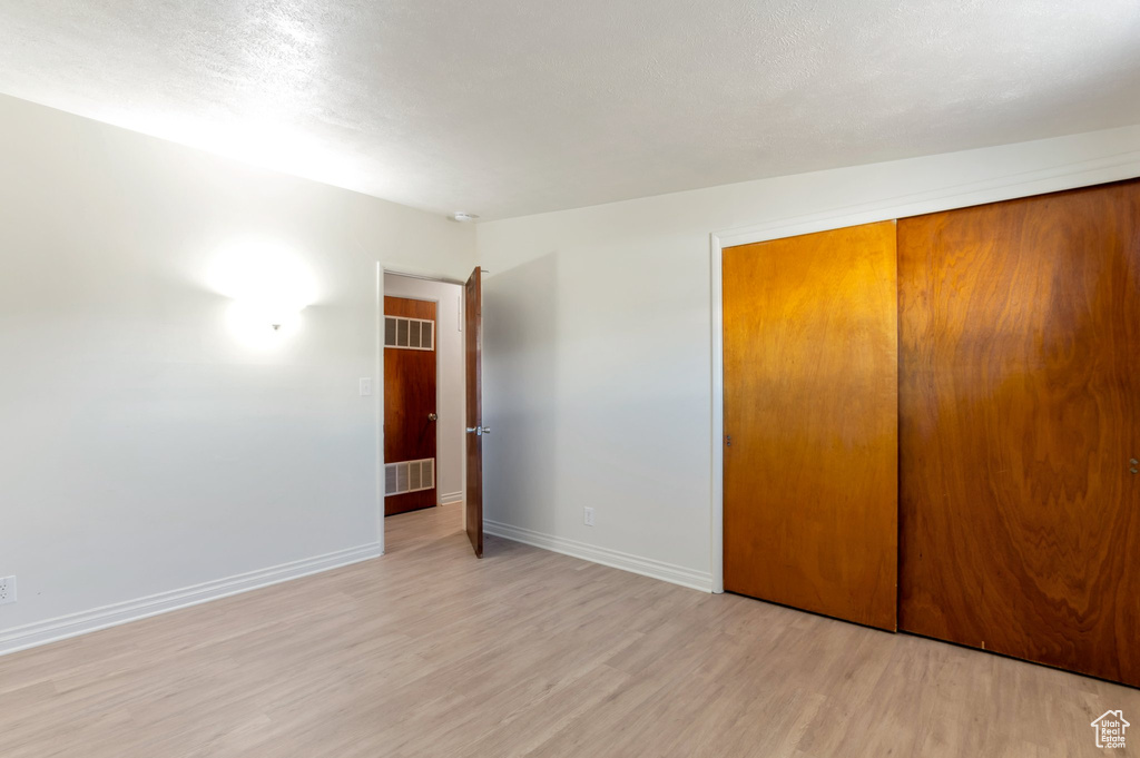 Unfurnished bedroom with light wood-type flooring, visible vents, a textured ceiling, a closet, and baseboards