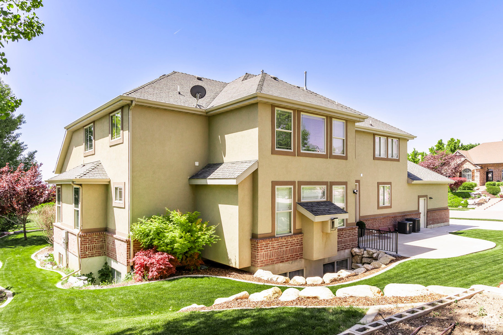Back of house with stucco siding, a patio, a yard, and brick siding