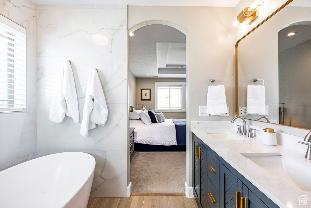 Full bath featuring double vanity, wood finished floors, connected bathroom, and a freestanding bath