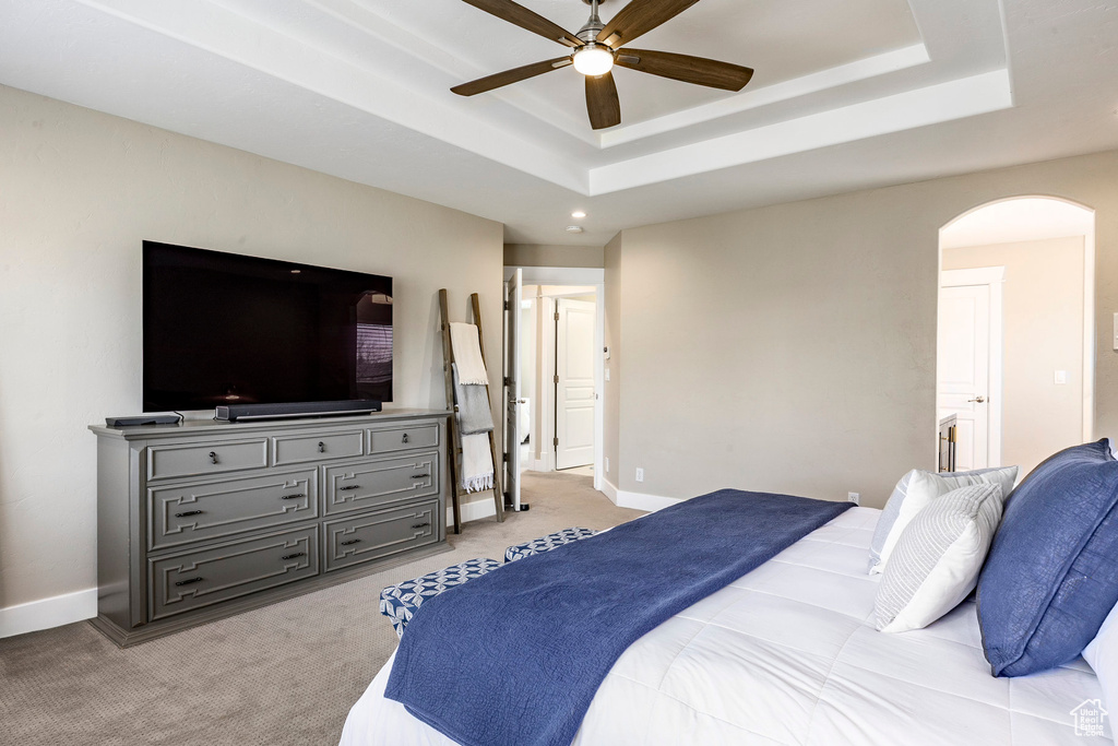 Bedroom featuring arched walkways, a raised ceiling, light carpet, baseboards, and a ceiling fan